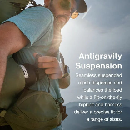 Person hiking with a backpack, wearing sunglasses and a cap, against a mountainous background.