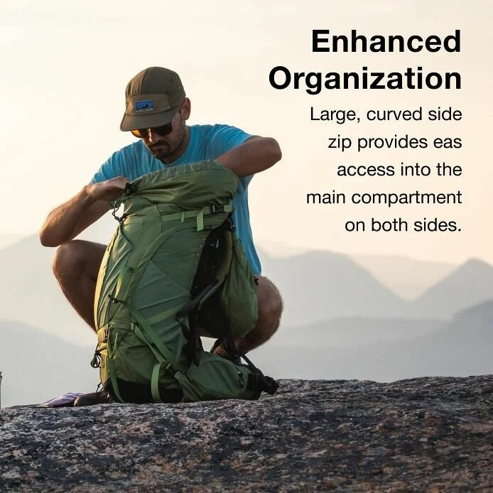 Man organizing a green backpack with mountains in the background