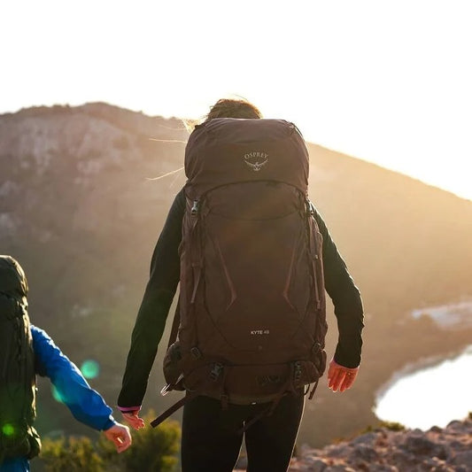 Two hikers with backpacks walking towards a mountainous landscape.