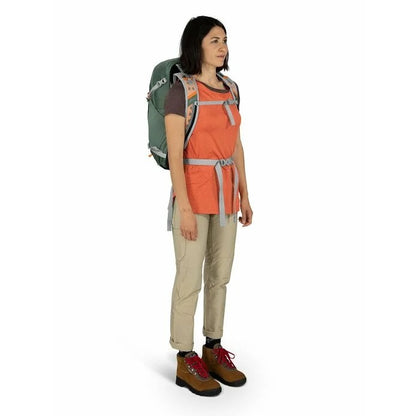 Woman wearing an orange shirt, beige pants, and a green backpack on a white background