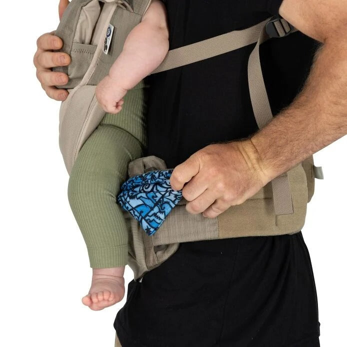 Person using a baby carrier with a baby wearing green pants and a blue patterned diaper.