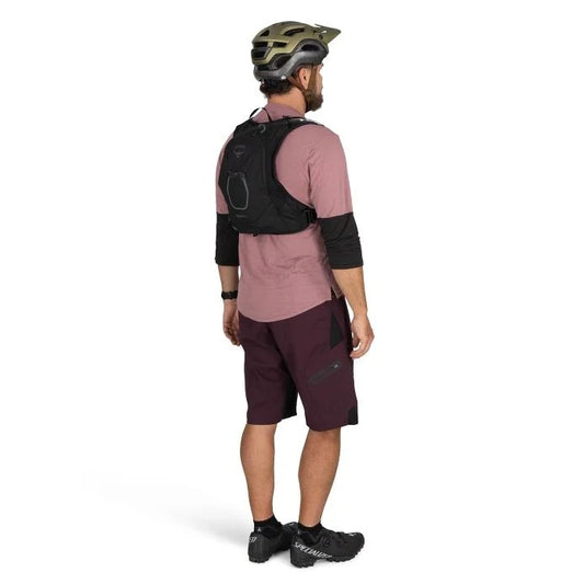 Person wearing a pink shirt, maroon shorts, black backpack, and helmet on a white background