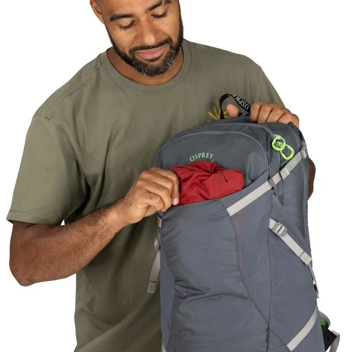Man opening a gray Osprey backpack with a red item inside on a white background