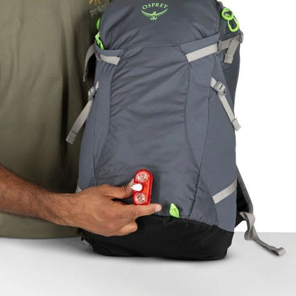 Person holding a red device next to a gray Osprey backpack on a white background