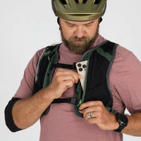 Man wearing a helmet and holding a phone in a green backpack against a white background