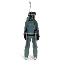 Person wearing a green ski suit and backpack with skis on a white background