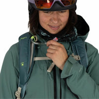 Person wearing a green jacket with a backpack, adjusting their helmet.