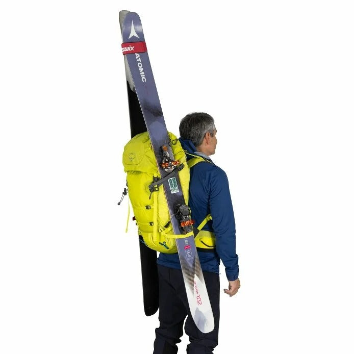 Person wearing a yellow backpack with skis on a white background