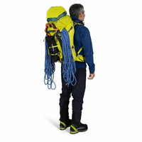 Person wearing a large yellow backpack with climbing equipment on a white background