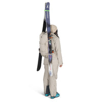 Person wearing a beige ski suit with skis attached to a backpack on a white background