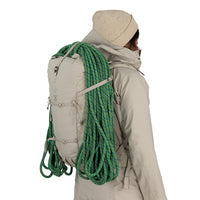 Person wearing a beige jacket with a backpack loaded with green climbing rope on a white background