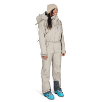 Person wearing a beige snowsuit with blue boots on a white background
