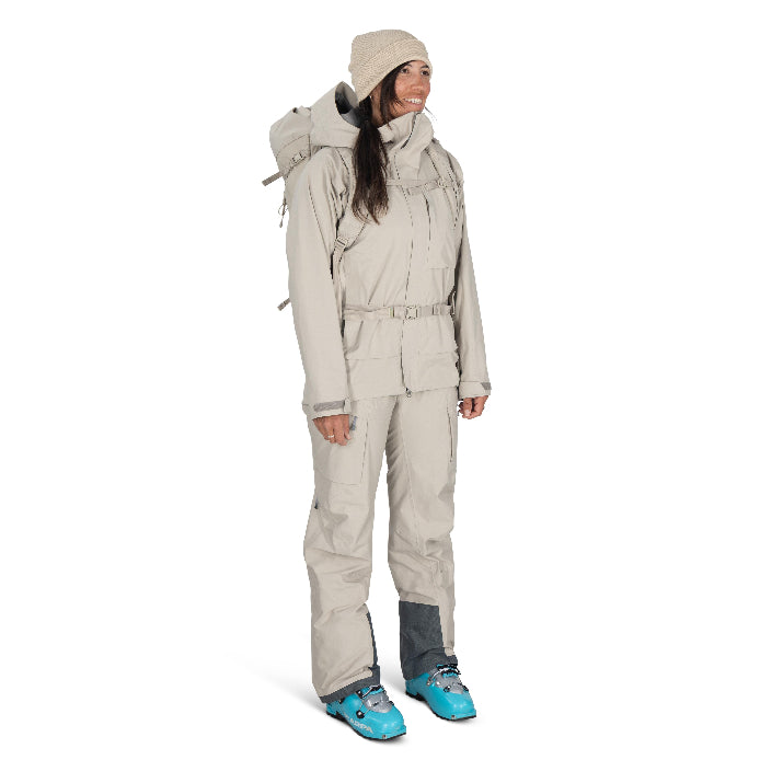 Person wearing a beige snowsuit with blue boots on a white background
