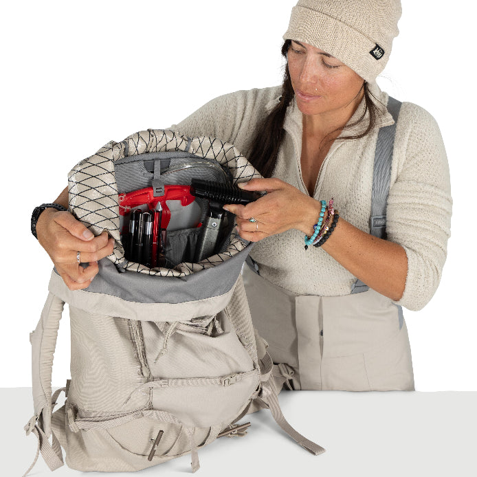 Woman organizing items in a beige backpack on a white background