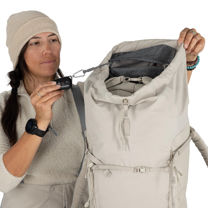 Woman holding a beige backpack with a small device, wearing a matching outfit.