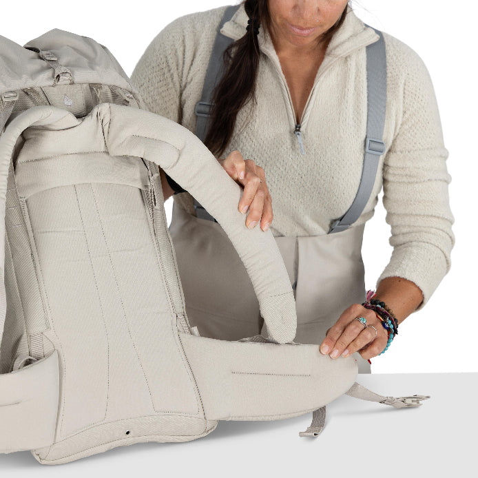 Person adjusting a beige baby carrier on a white background