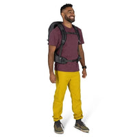 Man wearing a purple shirt, yellow pants, and a backpack on a white background