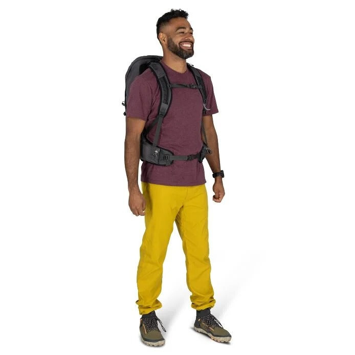 Man wearing a purple shirt, yellow pants, and a backpack on a white background