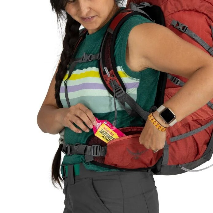 Person wearing a red backpack with a colorful striped shirt and holding a pink item.