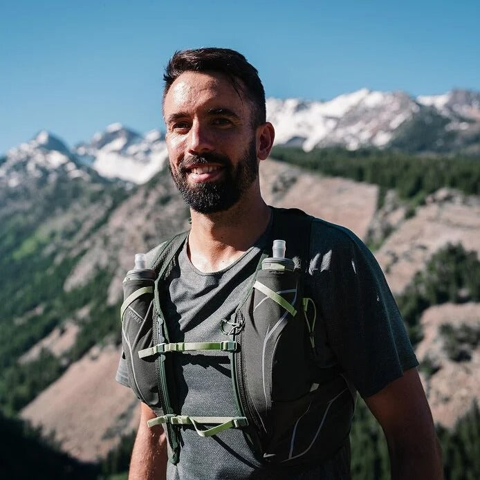 Man with a backpack and water bottles standing in front of mountains