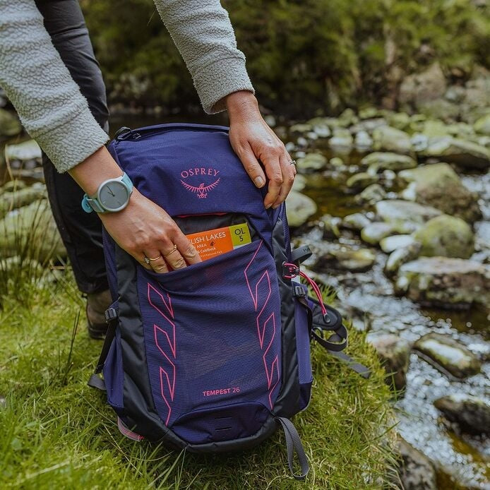Person holding a purple Osprey backpack by a stream