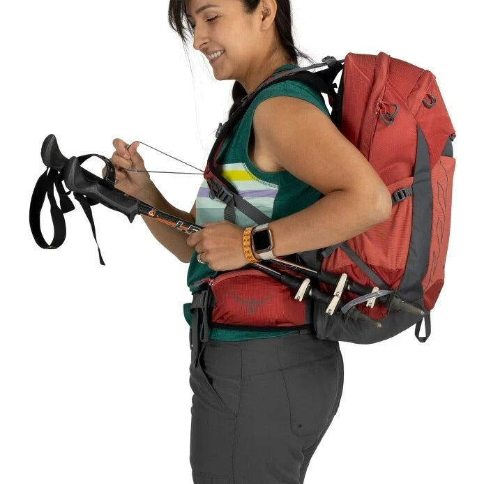 Person wearing a red and gray backpack holding archery equipment on a white background