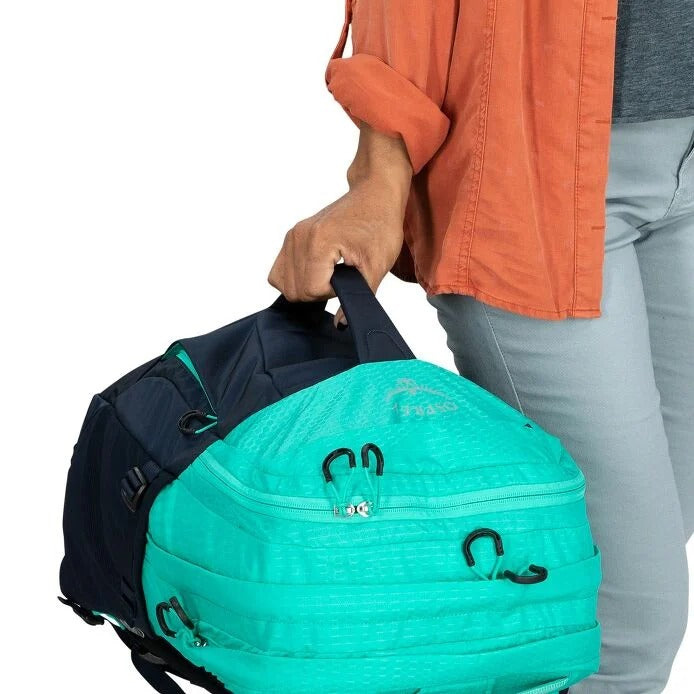 Teal 30L backpack with top zipper open as a hand places items inside