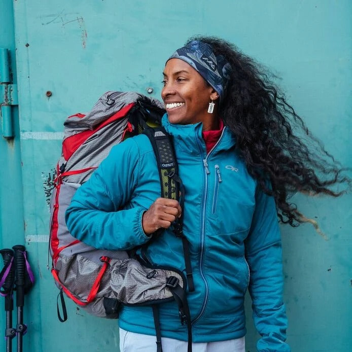 Woman in a blue jacket with a backpack against a teal wall