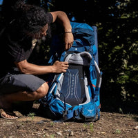 Person adjusting a blue Osprey backpack outdoors