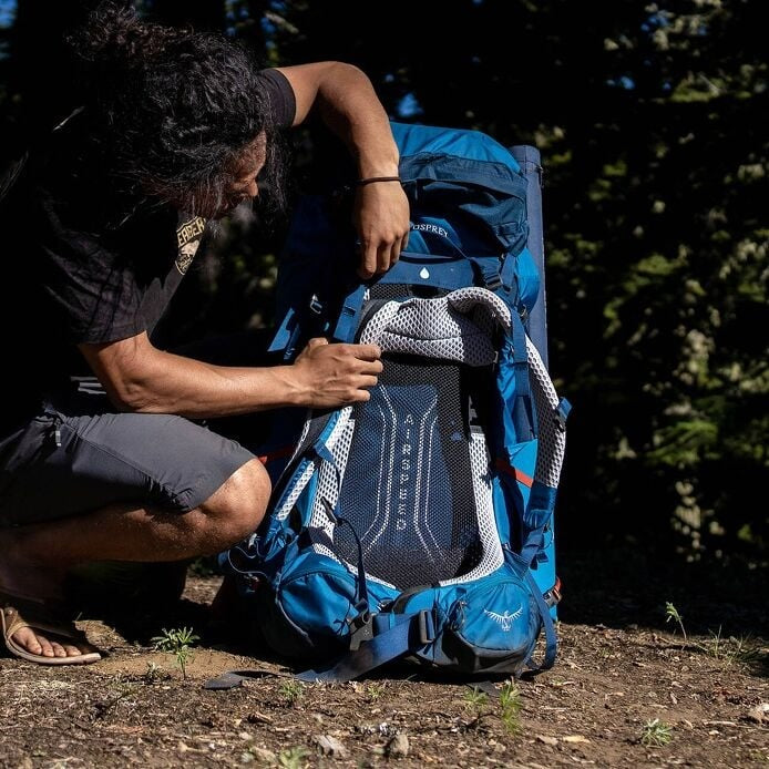 Person adjusting a blue Osprey backpack outdoors