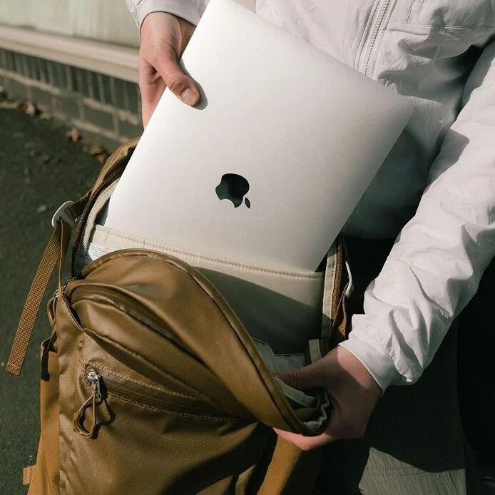 Person holding a laptop with an Apple logo in a brown bag outdoors.