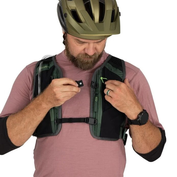Man wearing a green helmet and black backpack, adjusting something on the backpack.