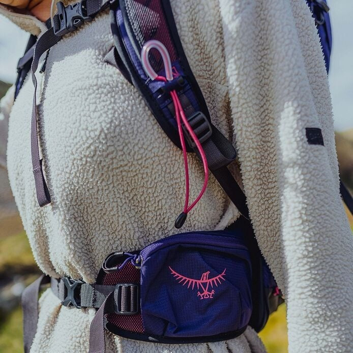 Person wearing a white fleece jacket with a blue and purple backpack featuring a logo.
