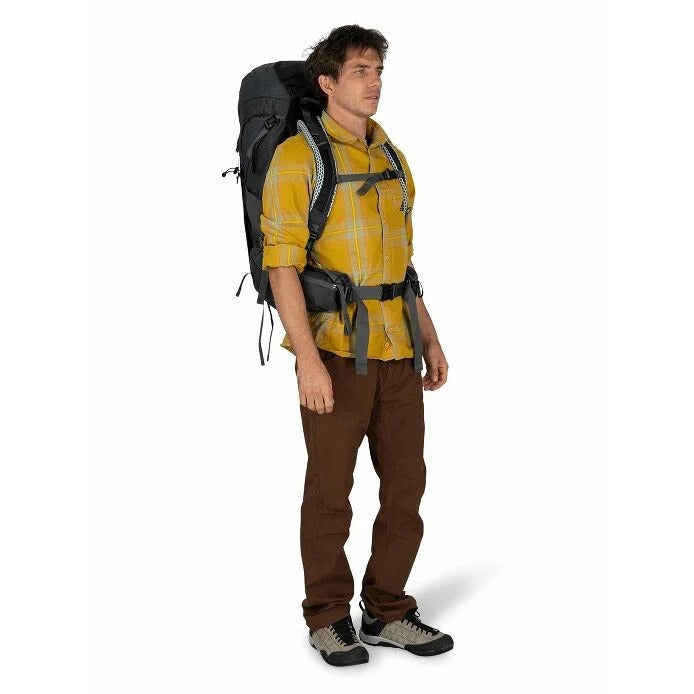 Man wearing a yellow plaid shirt, brown pants, and a large black backpack on a white background