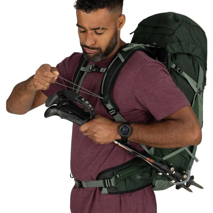Man with a green hiking backpack adjusting equipment on a white background