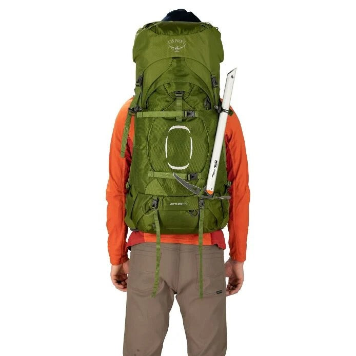 Person wearing a green backpack with orange jacket and brown pants on a white background
