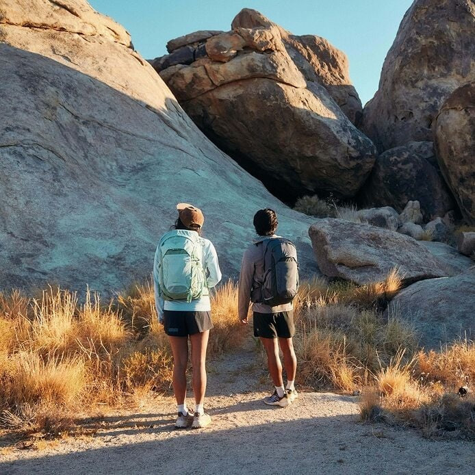Two people hiking on a rocky trail with backpacks.
