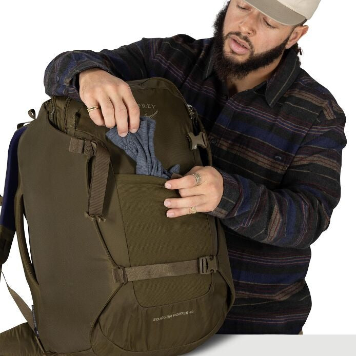 Olive green travel pack front pocket opened with hands adjusting an inner organizer