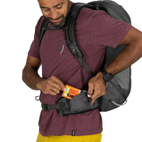 Man with a gray backpack holding an orange product against a white background