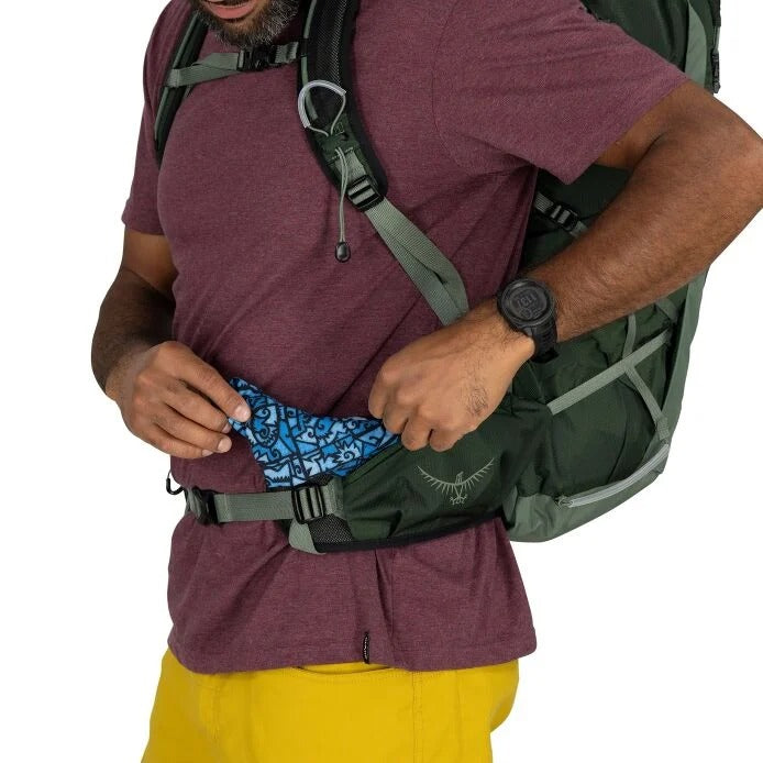 Man with a green backpack and purple shirt holding a blue patterned item.