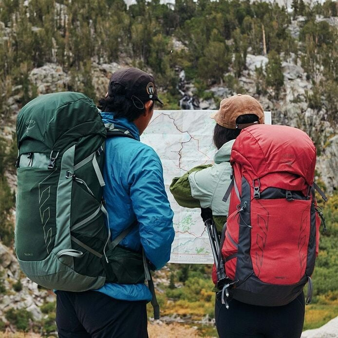 Two hikers with backpacks looking at a map in a mountainous area
