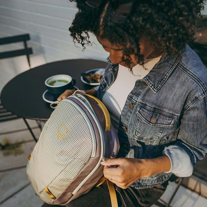 Person opening a backpack outdoors with a table and chair in the background