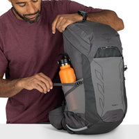 Man holding a gray backpack with an orange water bottle inside, on a white background
