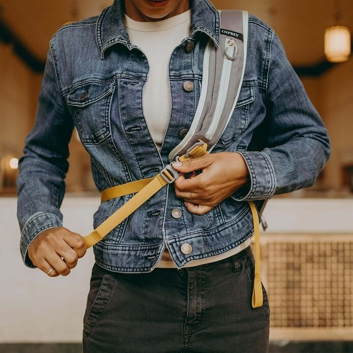 Person wearing a denim jacket with a backpack, adjusting the strap indoors.