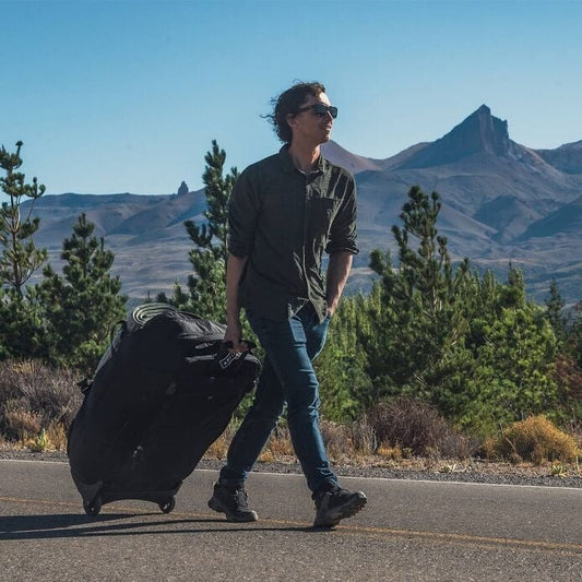 Person walking with a suitcase on a road with mountains in the background