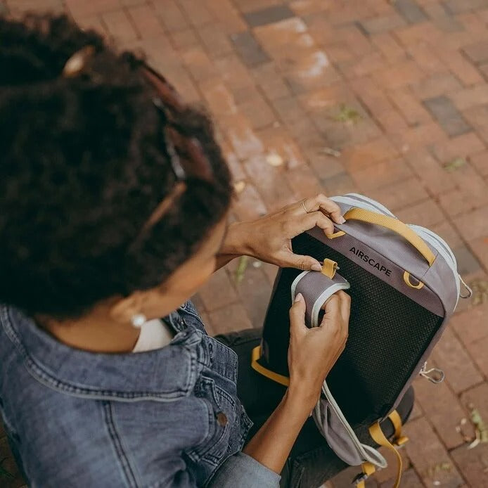 Person holding a black and yellow backpack with 'AIRSCAPE' branding on a brick pavement.