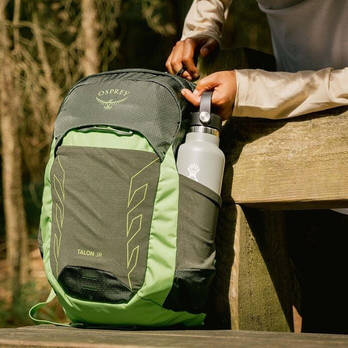 Green Osprey backpack with a water bottle on a wooden surface outdoors