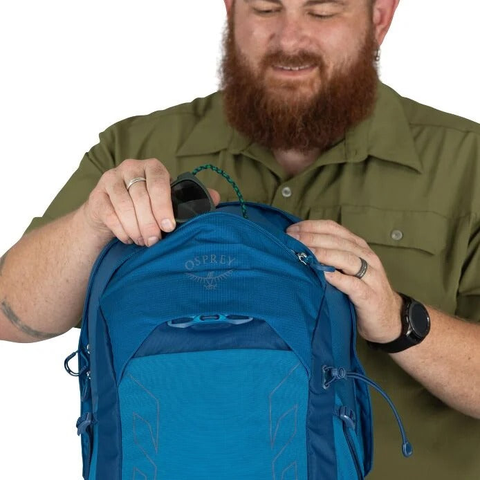 Man holding a blue Osprey backpack against a white background