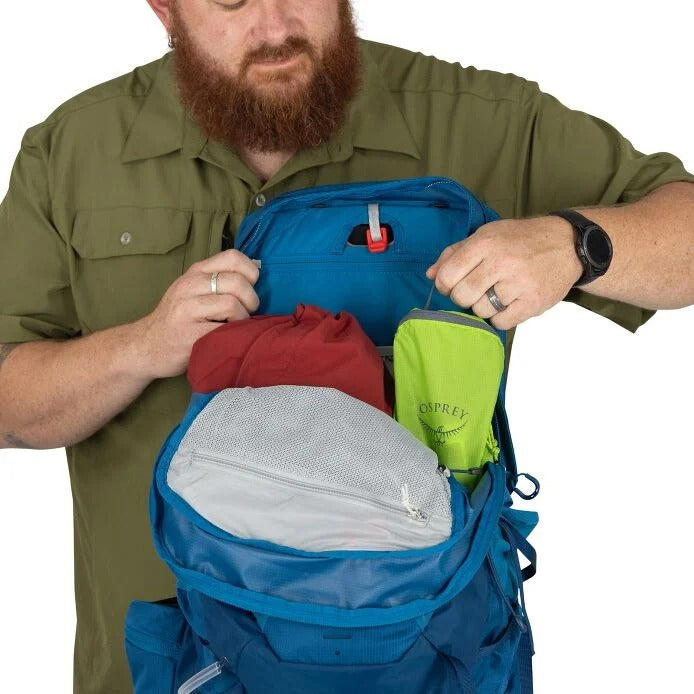 Man packing a blue backpack with various items on a white background