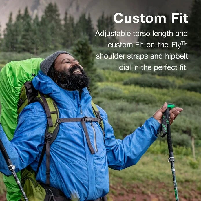 Man hiking with a green backpack and blue jacket, surrounded by nature.